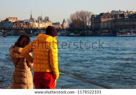 Couple (back view) admiring high water in Seine river at golden sunset. Winter flood in Paris, France.