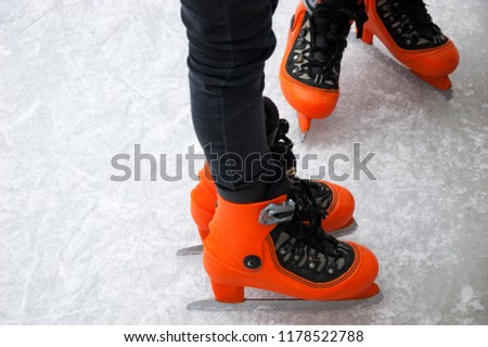 Two girls wearing orange skates on ice rink. Beginner skaters.
