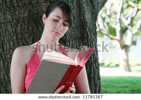 A cute young girl reading a book under the oak tree
