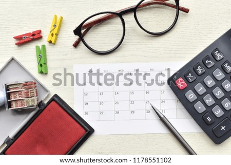Top view wooden table,Set calendar work have a glasses,a rubber stamp,a calculator,a paperclip,a pencil is office equipments