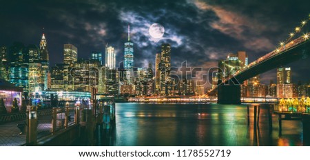 New York City Brooklyn Bridge and Manhattan skyline illuminated at night with full moon overhead.