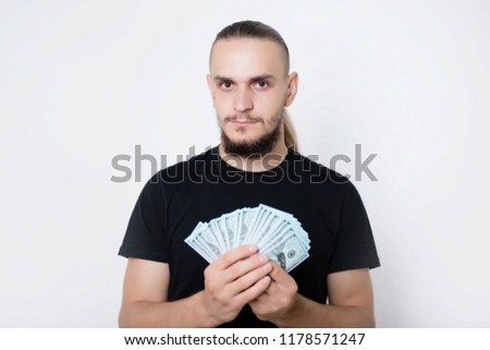 Young handsome guy in a black T-shirt on a white background holds dollars in his hands. Man with money
