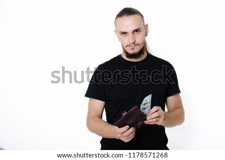 Young handsome guy in a black T-shirt on a white background holds dollars in his hands. Man with money