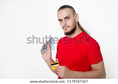 A young handsome guy in a red T-shirt on a white background holds a dollar and yellow card in his hand. Man with money and a bank card