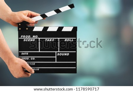 Cinema clapperboard in female hands on blue bokeh background