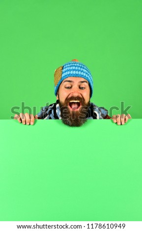 Man in warm hat looks down on green background, copy space. Hipster with beard and happy face wears warm clothes. Autumn and demi season clothes concept. October and November sale idea