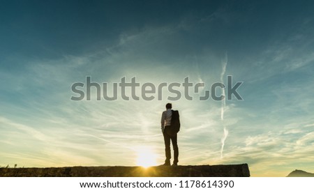Businessman standing on the skyline on a wall silhouetted against the sun with copyspace.