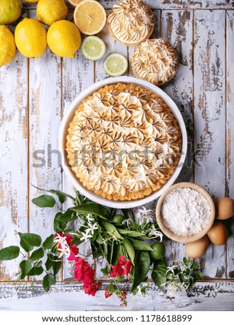 Lemon meringue pie served with lemons and flowers over white wooden background. Top view