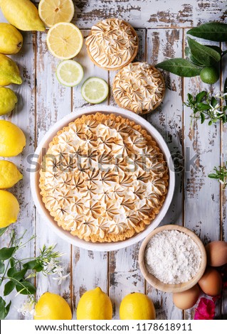 Lemon meringue pie served with lemons and flowers over white wooden background. Top view