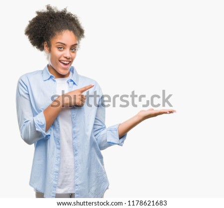 Young afro american woman over isolated background amazed and smiling to the camera while presenting with hand and pointing with finger.