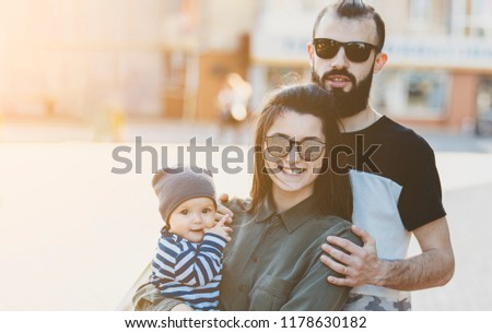Happy young family. Stylish bearded man and young beautiful wife with a little child in their arms, hugging, kissing and playing walking around the city.