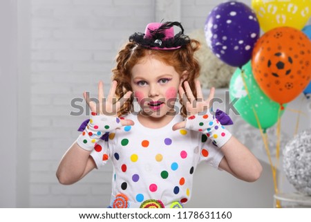 red-haired girl in the image of a clown, shows his hands. . In a white room with balloons.