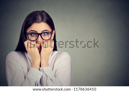 Unsure anxious woman biting her fingernails feeling nervous isolated on gray background. Negative human emotions
