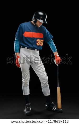 Tired hitter in full length portrait. Guy dressed in a team uniform, lowered his head and leant on a baseball bat.
