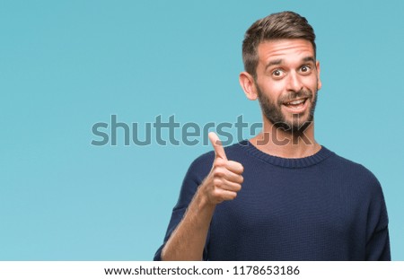 Young handsome man wearing winter sweater over isolated background doing happy thumbs up gesture with hand. Approving expression looking at the camera with showing success.