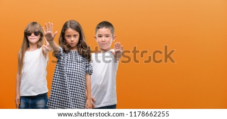 Group of boy and girls kids over orange background with open hand doing stop sign with serious and confident expression, defense gesture
