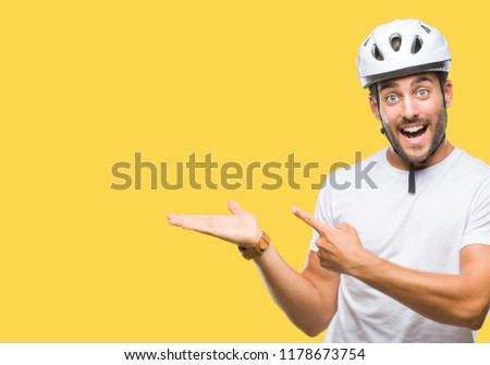Young handsome man wearing cyclist safety helmet over isolated background amazed and smiling to the camera while presenting with hand and pointing with finger.