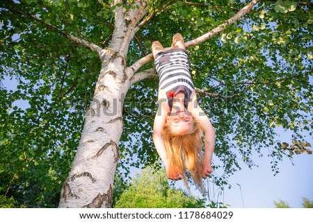 Low angle view of happy girl hanging  upside down from a birch tree looking at camera enjoying summertime Royalty-Free Stock Photo #1178684029