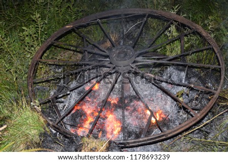 Antique metal carriage wheels burning in a meadow.