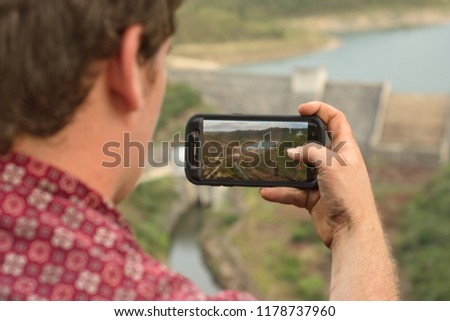 a man taking pictures of a dam with a smartphone 