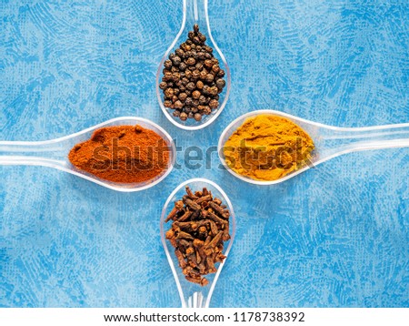 Assortment of dry spices on spoons isolated on a textured blue background. Four spoons with spicy ingredients on texture background, space for text, multiple colors Royalty-Free Stock Photo #1178738392