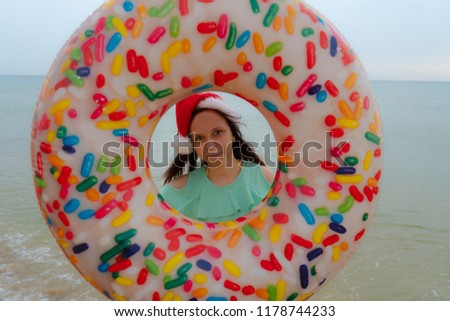 Beautiful girl on the beach in a cap, like Santa Claus, holding an inflatable circle in the form of a donut. Concept-holiday for Christmas.
