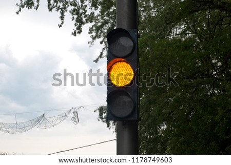 yellow traffic light (background: cloudy sky, trees)