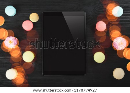 Digital tablet, macarons and pink beautiful flowers on wooden background. Colored hightlights effects