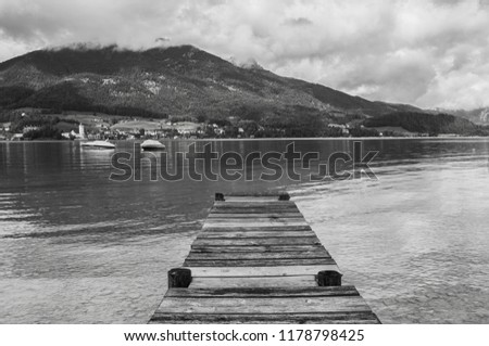 Black and white photo of wooden deck in the cold lake in austrian alps with misty mountains and hills in the background
