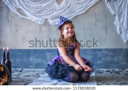 girl in the witch costume frightens. child is celebrating Halloween. Scary spider on the wall. Cut black pumpkin. Decor for Halloween.