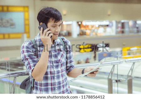 traveller with world map in hand and using mobile phone in the airport background. Handsome caucasian man,  tourism, or holiday vacation travel concept. 