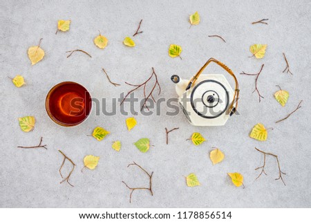 Warm tea on a cool autumn day. Teacup, teapot and fallen leaves on concrete background.