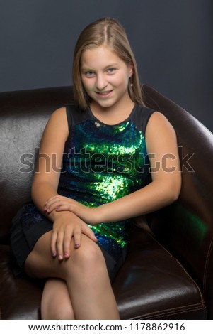Beautiful teen girl sits in the studio on a leather chair. Concept of youth fashion and culture.