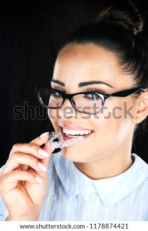 Stomatology concept, head and shoulders of woman with strong white teeth looking at camera and smiling, holding false tooth, denture. Young woman at dentist's, Invisalign orthodontics