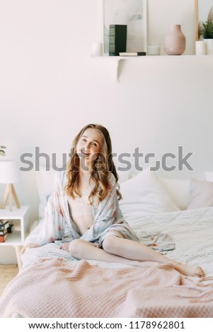 Girl in the early morning in bed and Bathrobe, wakes up and getting ready to work. Productive day. Smiles and laughs. Lying in bed, catching the sunrise. Happy morning in the bedroom.