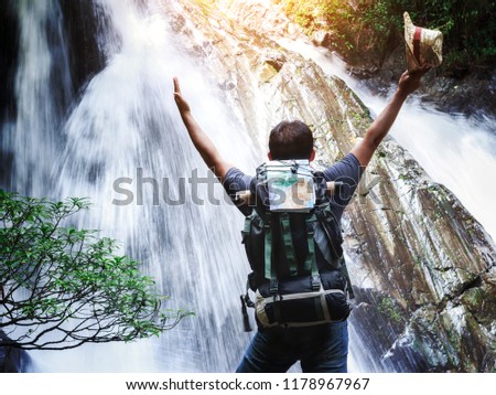 male hiker with raised hands and waterfall background