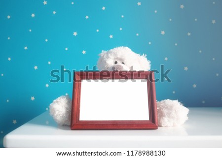 Empty photo wooden frame and white teddy bear in the beautiful blue starry nursery
