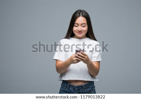 Portrait of a cheerful asian woman holding mobile phone and looking at camera isolated over gray background