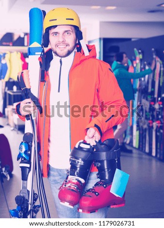 Cheerful guy in skiing outfit satisfied with choice in modern store of sports equipment