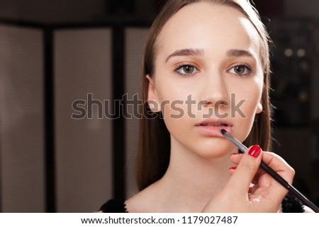 makeup artist applying a lip gloss on lips of a young pretty girl. concept of professional make up couching Royalty-Free Stock Photo #1179027487