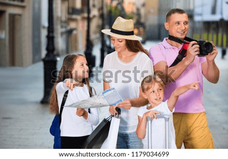 Happy positive  tourist family using map and taking photo of city while strolling with camera and phone 