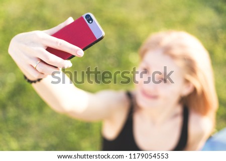 A blonde girl in a black T-shirt is resting in the nature and taking pictures of herself on the phone