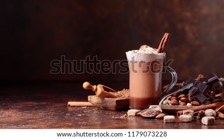 Cocoa with cream, cinnamon, chocolate pieces and various spices on a brown background. Copy space for your text.