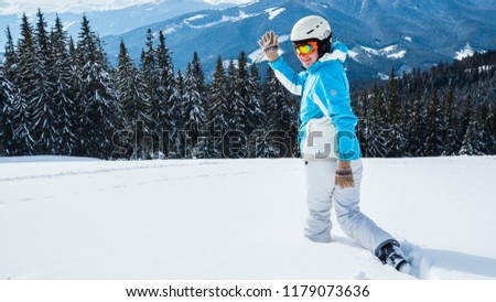 Woman skier in a white and blue suit at the mountain top in snow.