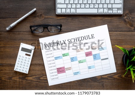 Weekly schedule. Planning the week. Multicolored planner on manager, marketologist's dark wooden office desk with computer keyboard and calculator top view