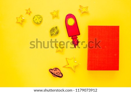Literature for children. Fantactic, fiction story. Book with blank cover near cutout of rocket, stars, moon on yellow background top view mockup copy space