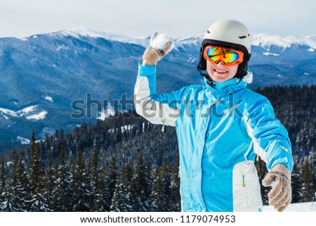 a woman in a blue ski suit and mask hurls snow at the camera on top of the mountain.the girl throws snow at the camera