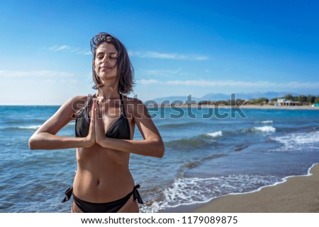 Beautiful young female doing yoga on beach. Gorgeous woman in bikini meditating on beach at summertime on vacation