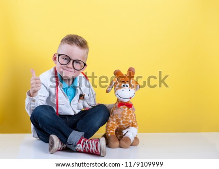 Child playing doctor with toy animal giraffe. Happy smiling kid boy with thumb up at home or daycare. Pediatrician for preschool and kindergarten kids. Pediatric, healthcare and people concept.