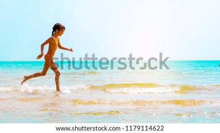 Picture of exciting little girl running on beach beside waves. Vintage image of kid in day sunlights on seaside background.
